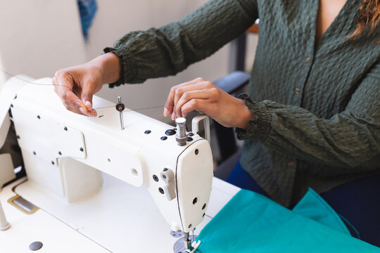 Biracial female fashion designer using sewing machine in sunny studio