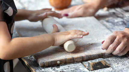 The hands of the mother and child roll out the dough with a rolling pin on the table