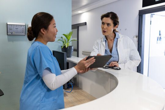 Diverse female doctors with tablet talking across hospital reception desk