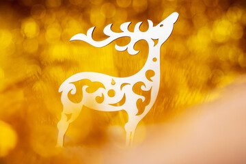 A decorative white reindeer cut out of plywood on a blurred golden bokeh background, the reindeer...