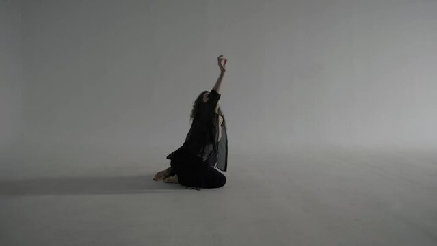 Curly beautiful woman in black clothes dances on the floor on a cyclorama in a white photo studio