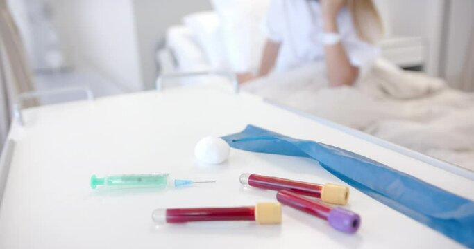 Syringe and blood samples on table, and defocused patient in hospital bed, slow motion
