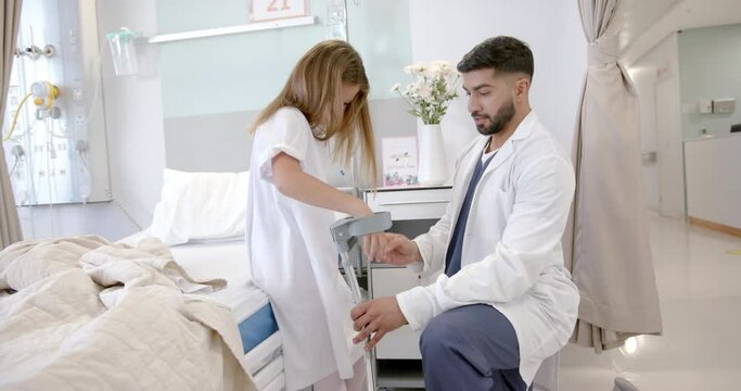 Diverse male doctor adjusting crutches for girl patient in hospital ward, slow motion