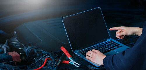 Hands of auto mechanic using computer for diagnostics engine working and repairing car in a garage. Blur repair service in background. wide panoramatic banner with empty space for copy text.