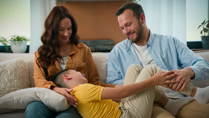 Happy caucasian family dad mom with cute kid son tickling having fun relax on sofa together...
