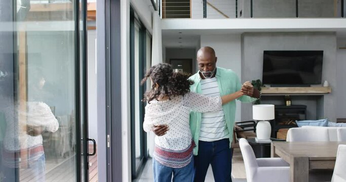 Happy biracial couple holding hands and dancing in living room, slow motion