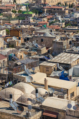 Chaotic rooftop view of a city in the Middle East featuring satellite dishes and water tanks