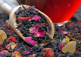 black blended tea with flower petals and dried fruit on a wooden scoop. close up
