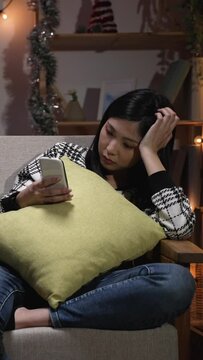 Vertical Screen: asian woman sitting couch in the living room. and addicted to cell phone neglecting her unhappy boyfriend at home in the evening