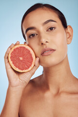 Woman face, grapefruit for vitamin C and natural skincare or diet against a blue studio background. Portrait of female person with organic citrus fruit for nutrition, dermatology or healthy wellness