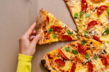 Female hand takes a piece of pizza. High angle view of pizza with pepperoni and basil.