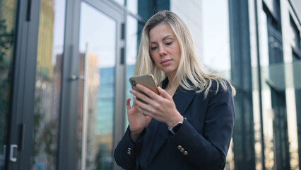 Serious confident 40s girl text message. Successful 30s business woman type job sms. Sexy boss lady use mobile cell phone chat close up. Pretty top manager walk. Blond hair person wear city work suit.