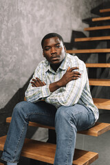 Obraz premium Young african man sitting on a wooden ladder in a room, portrait