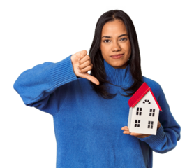 Young Filipina woman holding a miniature house showing a dislike gesture, thumbs down. Disagreement concept.