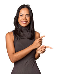 Young Filipina with long black hair in studio excited pointing with forefingers away.