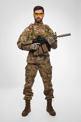 Confident, serious military officer carrying assault weapon with both hands in studio. Front view...