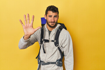 Young Hispanic man ready for hiking smiling cheerful showing number five with fingers.