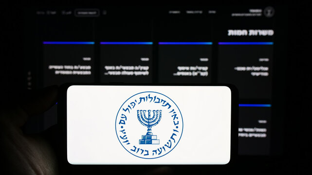 Stuttgart, Germany - 10-29-2023: Person holding mobile phone with logo of Israeli national intelligence agency Mossad in front of web page. Focus on phone display.