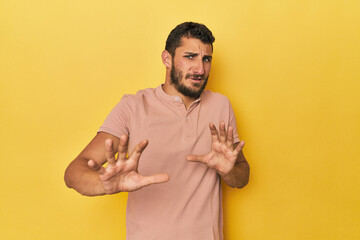 Young Hispanic man on yellow background rejecting someone showing a gesture of disgust.