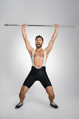 Happy male powerlifter screaming, while lifting unweighted barbell. Front view of cheerful athlete in singlet training, isolated on white studio background. Concept of weightlifting, powerlifting.