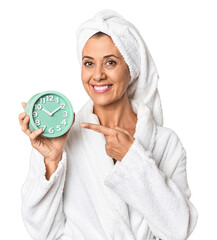 Middle-aged woman in bathrobe holding alarm in studio