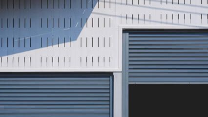 Roller shutter doors with white ventilated fiber cement smart board wall of warehouse building with sunlight and shadow on surface