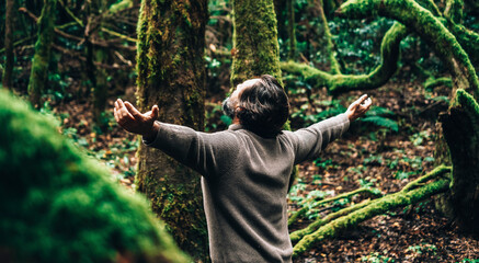 Freedom and happiness healthy lifestyle and nature lover people concept with back view of man opening outstretching arms in the forest with green ambient and trees around. Environment protection adult