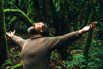 One man outstretching arms in the green dark forest. Environment and travel destination concept lifestyle. People in outdoors leisure activity enjoying breathing in the woods. Climate change warming - obrazy, fototapety, plakaty