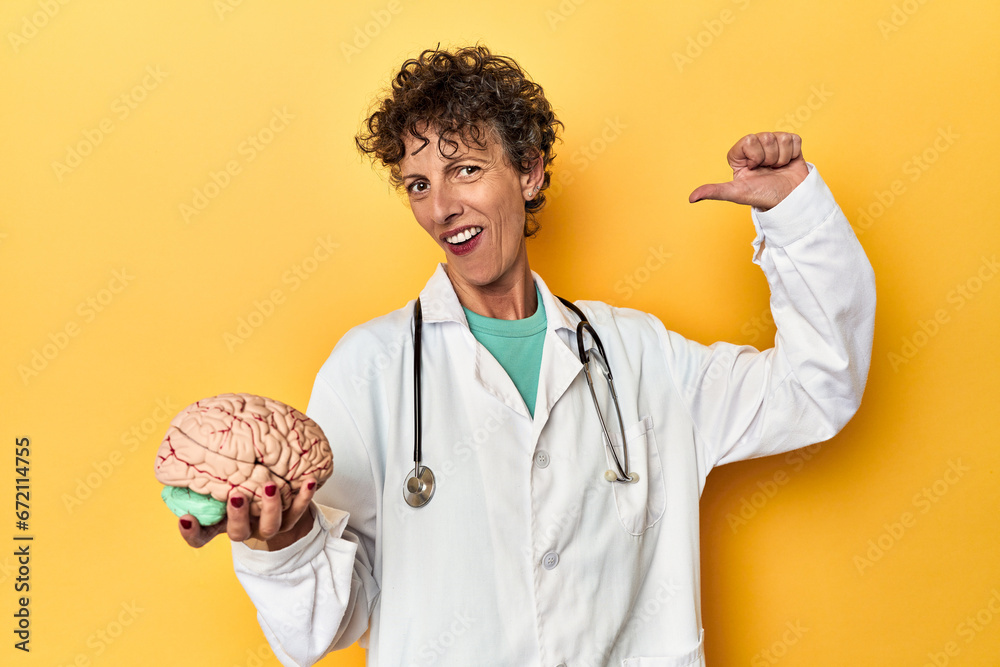 Wall mural doctor holding a brain model on yellow studio feels proud and self confident, example to follow.