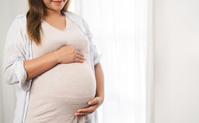 close up of a beautiful young woman during the third trimester of pregnancy Pregnant woman with arms on round belly, smiling, relax expression.
