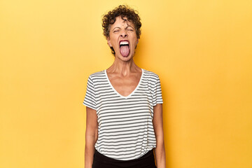 Mid-aged caucasian woman on vibrant yellow funny and friendly sticking out tongue. - Powered by Adobe