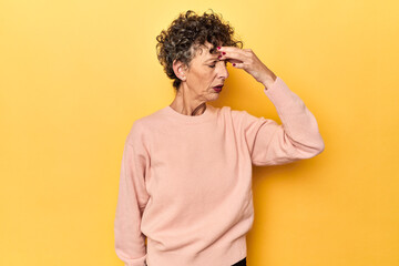 Mid-aged caucasian woman on vibrant yellow having a head ache, touching front of the face.