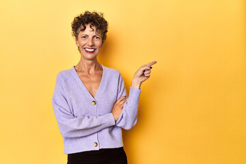 Mid-aged caucasian woman on vibrant yellow smiling cheerfully pointing with forefinger away.