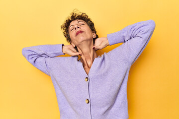 Mid-aged caucasian woman on vibrant yellow feeling confident, with hands behind the head.