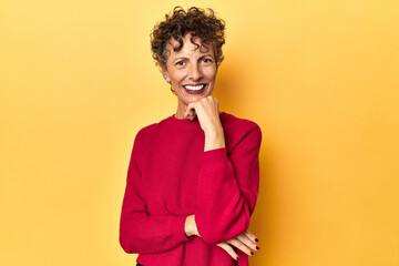 Mid-aged caucasian woman on vibrant yellow smiling happy and confident, touching chin with hand.