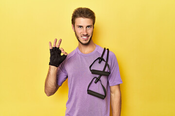 Athlete with resistance band on yellow cheerful and confident showing ok gesture.