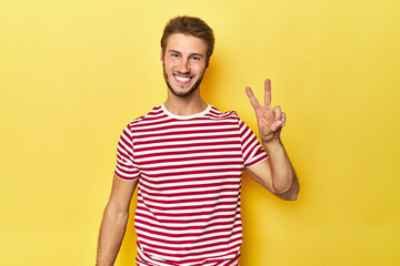 Young Caucasian man on a yellow studio background showing number two with fingers. - obrazy, fototapety, plakaty