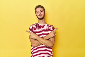 Young Caucasian man on a yellow studio background points sideways, is trying to choose between two options.