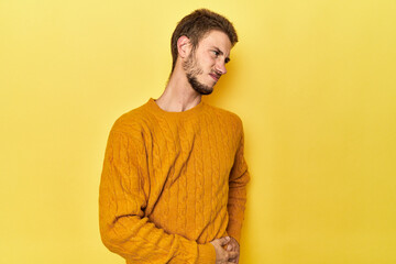 Young Caucasian man on a yellow studio background suffering a back pain.