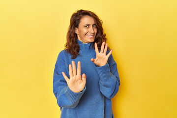 Middle-aged woman on a yellow backdrop rejecting someone showing a gesture of disgust.