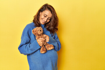 Pregnant woman holding teddy bear on yellow
