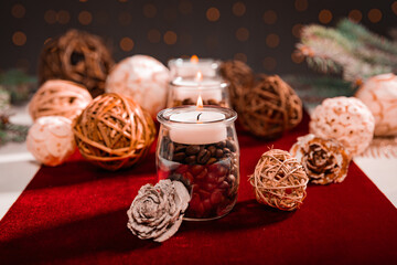 candles standing on wood among white-brown balls with white-red accessories on a dark background and branches of a Christmas tree