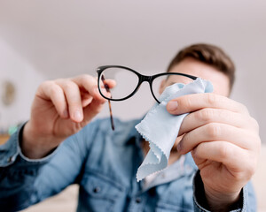 Man Cleaning Eyeglasses with Cloth, Focused on Maintenance and Care