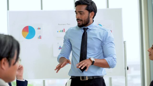 Young indian business manager standing and presenting to multiracial group of diversity colleagues in front of white board in meeting at boardroom in office . leader