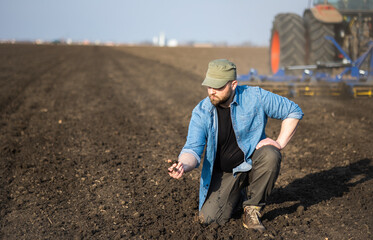 Farmer examing dirt while tractor is plowing field