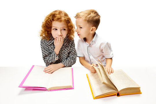 Cute redhead, curly girl sitting at desk with emotion of surprise while reading book. Child study and learn for preschool. Online education. Concept of childhood, International Knowledge Day. ad