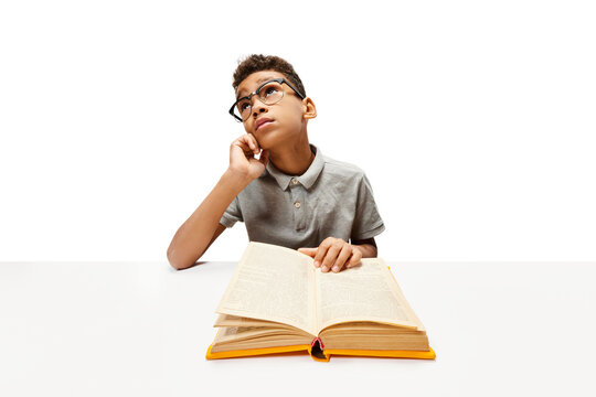 Dreaming African-American boy, pupil sitting with opened book, doing homework. Child study and learn for preschool. Online education. Concept of childhood, International Knowledge Day. Copy space, ad