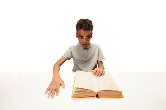 Surprised African-American boy sitting doing homework, reading exciting story. Child study and learn for preschool. Online education. Concept of childhood, International Knowledge Day, academic. ad