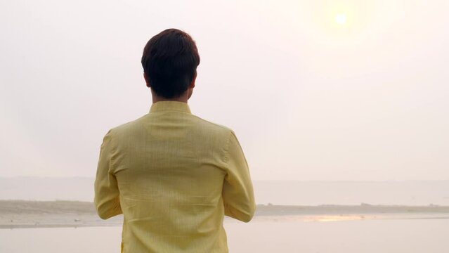 Shot of a young man celebrating chhath pooja - worshiping Lord Sun in the morning. A Hindu devotee standing in a river and praying for chhath pooja - Chhath festival