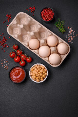 Raw chicken eggs in a box, cherry tomatoes, chickpeas, spices, salt and herbs